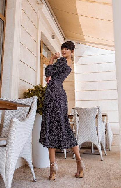 Woman in a long dark dress standing on a patio with white chairs and tables.