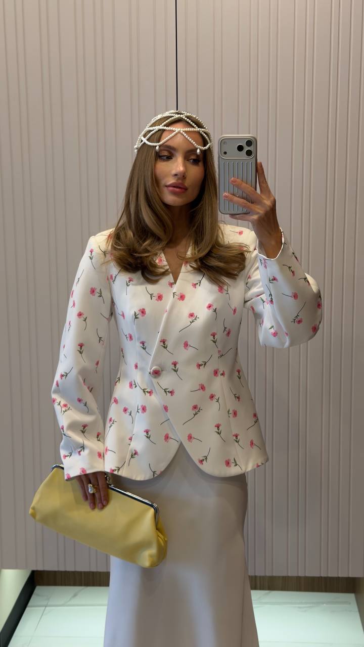 Woman taking a mirror selfie wearing a floral blouse and holding a yellow clutch.