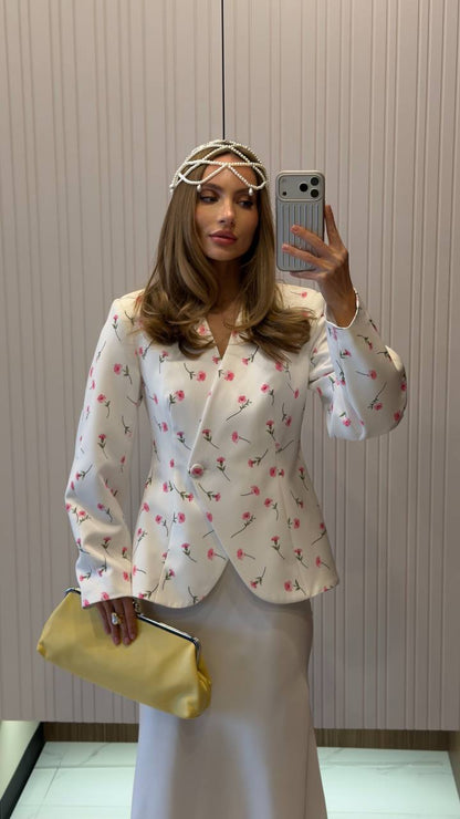 Woman taking a mirror selfie wearing a floral blouse and holding a yellow clutch.