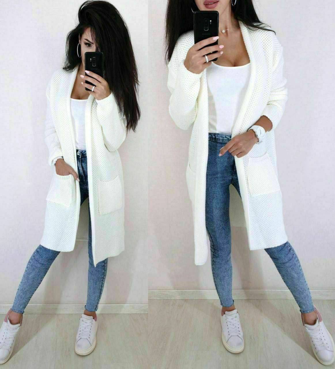 Woman wearing a long white cardigan, white top, blue jeans, and white sneakers.