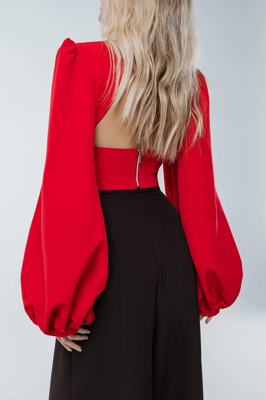 Red blouse with puffed sleeves and black pants on a plain background