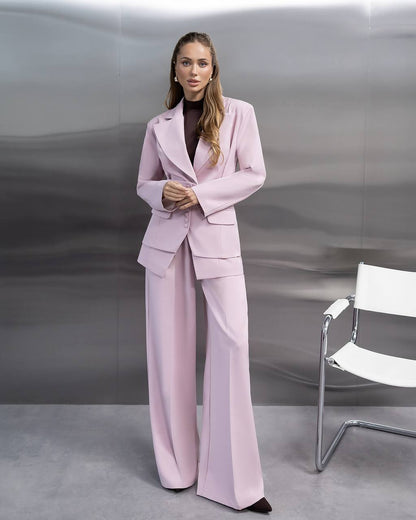 Woman in a pink suit standing in front of a gray background with a white chair.