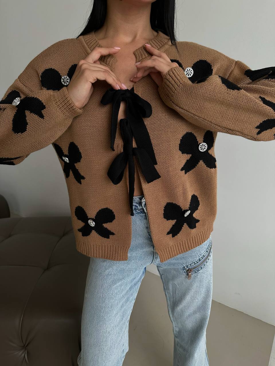 Person wearing a brown sweater with black bow designs and light blue jeans.