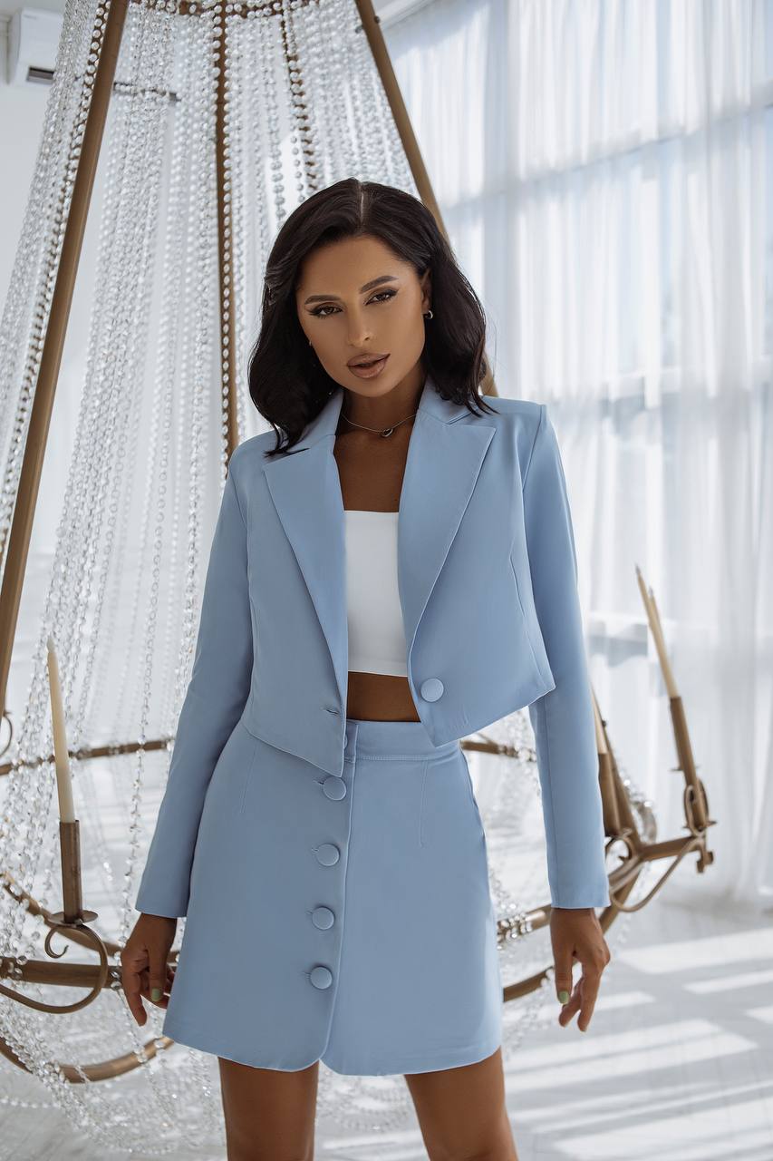 Woman in a light blue suit standing in a decorative indoor setting with large windows.
