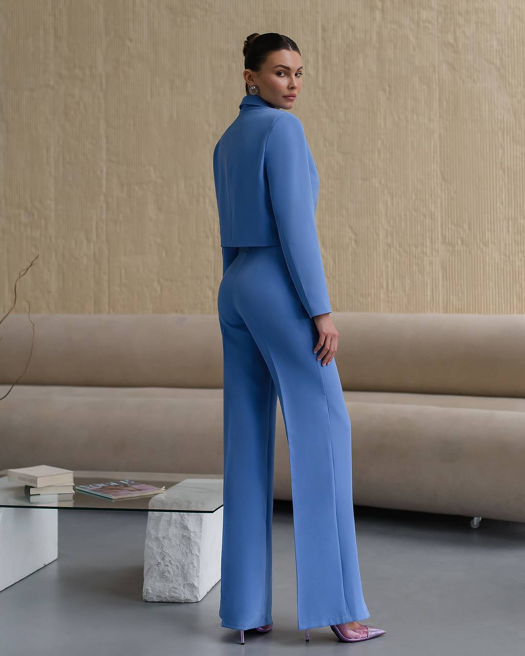 Woman in a blue suit standing in a room with a beige sofa and glass coffee table.