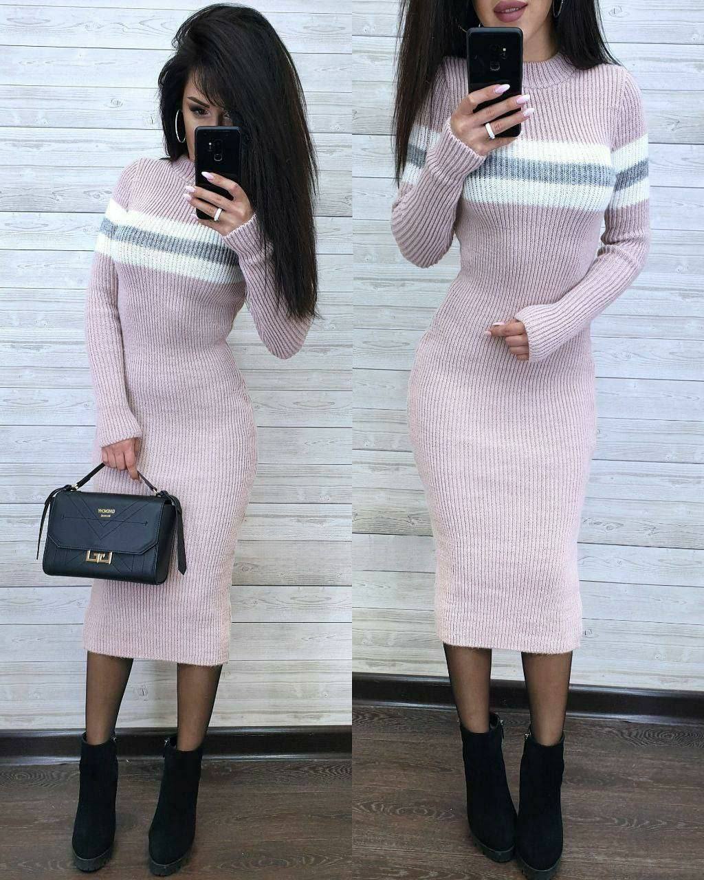 Woman wearing a pink sweater dress with striped pattern, holding a black handbag.