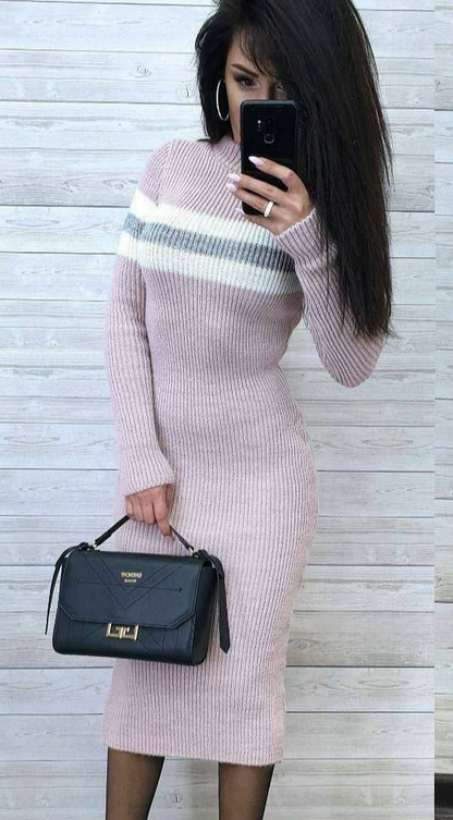 Woman wearing a pink ribbed dress with a striped pattern, holding a black handbag against a light wooden panel background.