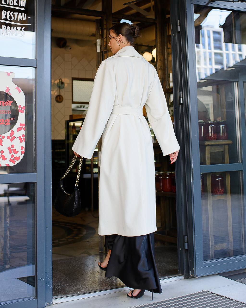Woman in a white coat walking out of a building with glass doors.