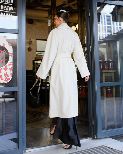 Woman in a white coat walking out of a building with glass doors.