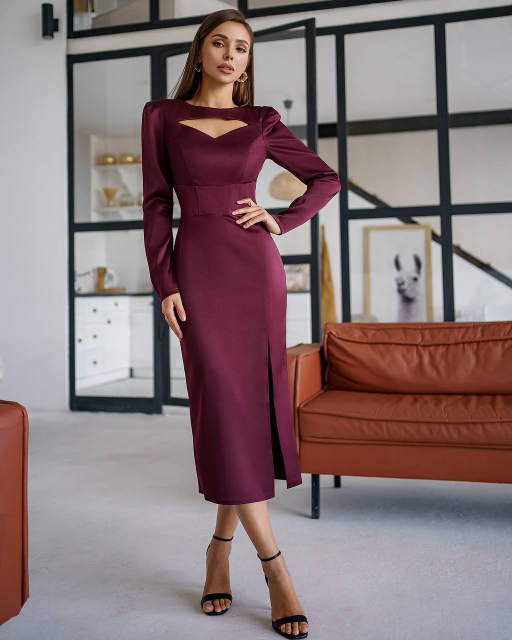Woman in a burgundy dress posing in a modern living room.