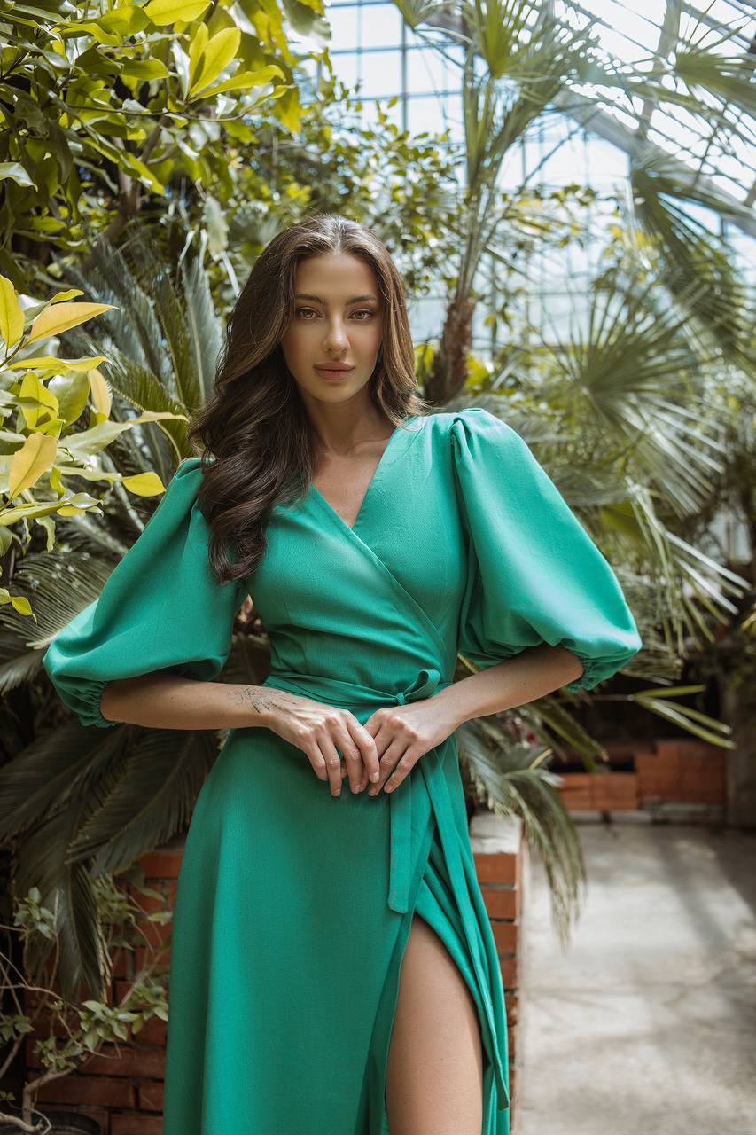 Woman in a green dress standing in a lush, green indoor garden.