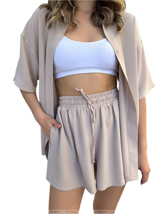 Woman wearing a beige cardigan, white sports bra, and beige shorts on a white background