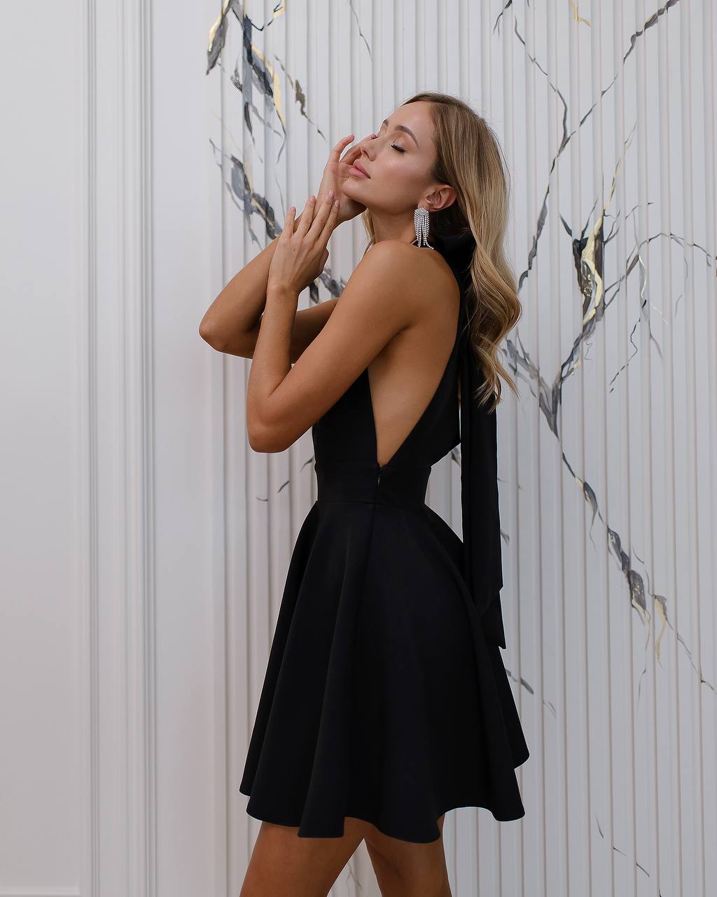 Woman in a black dress posing against a marble wall.