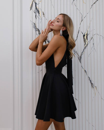 Woman in a black dress posing against a marble wall.
