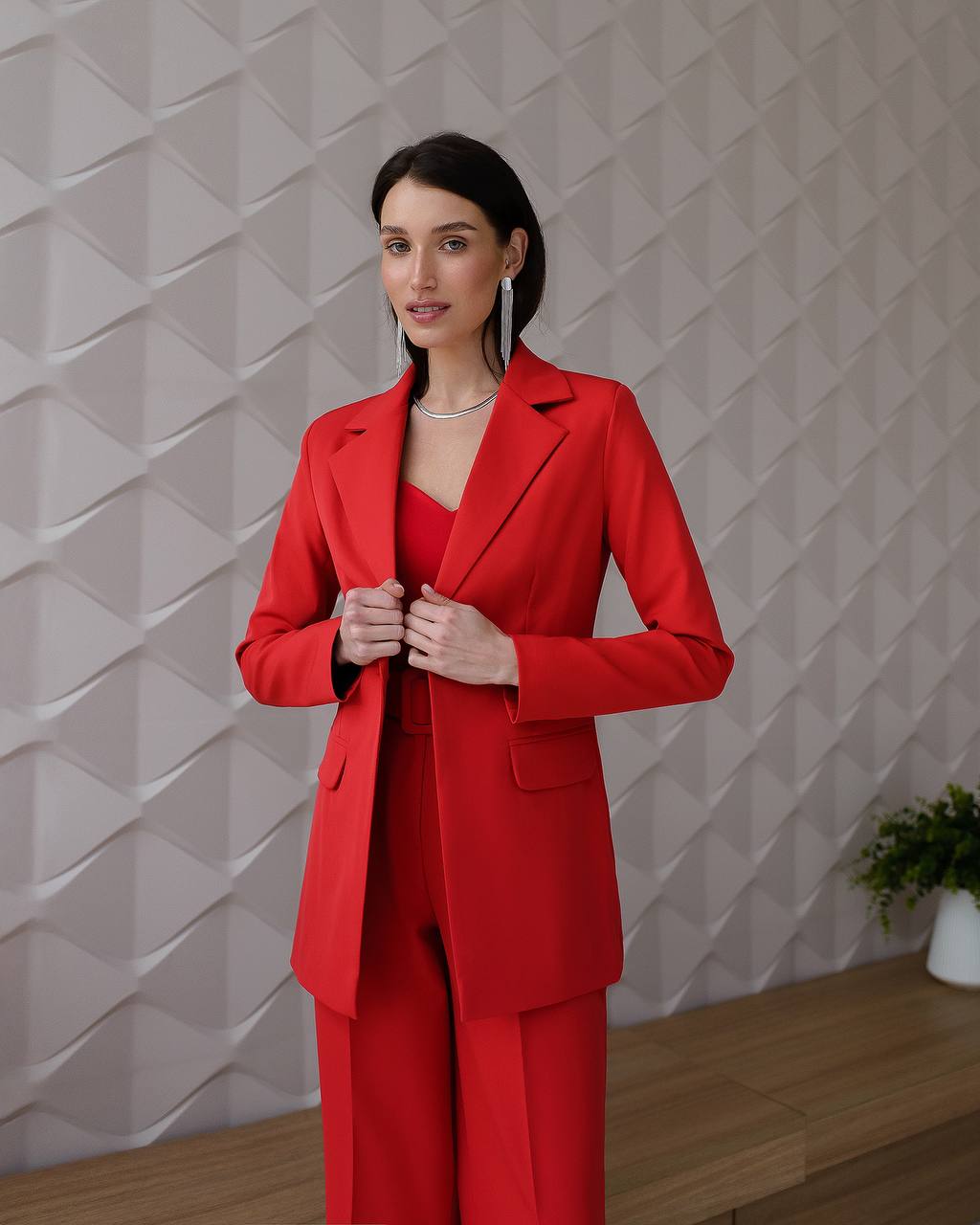 Woman wearing a red suit standing against a textured wall.