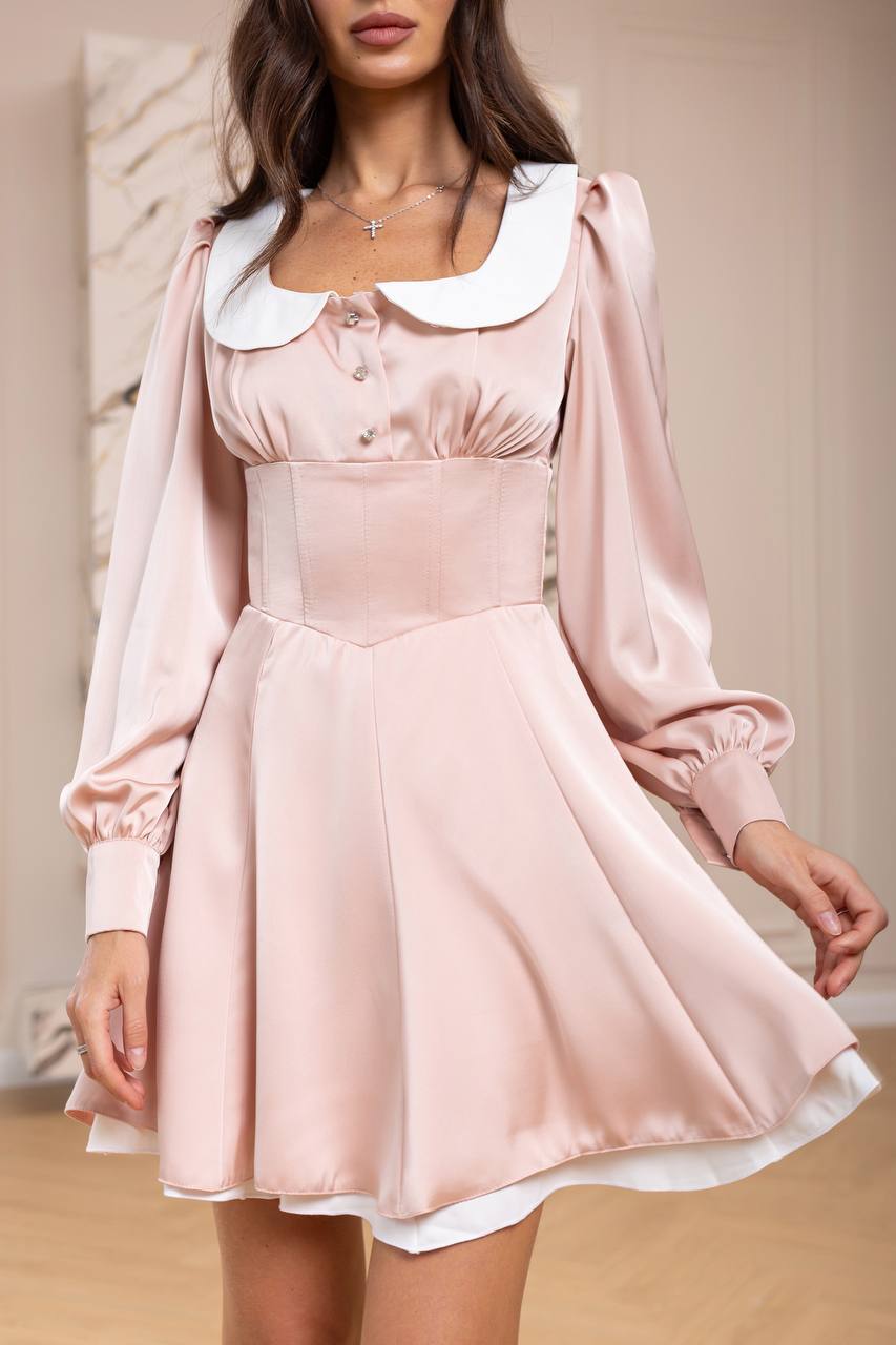 Woman wearing a pink dress with a white collar in an indoor setting