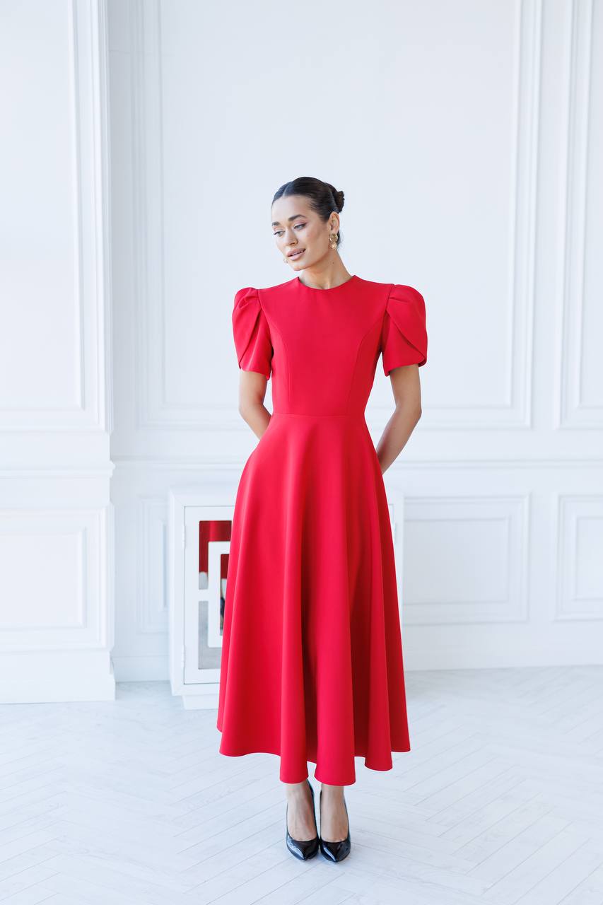 Woman wearing a red dress with puff sleeves in a white room.