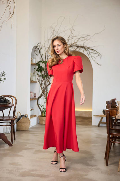 Woman in a red dress standing in a room with wooden furniture and decorative plants.