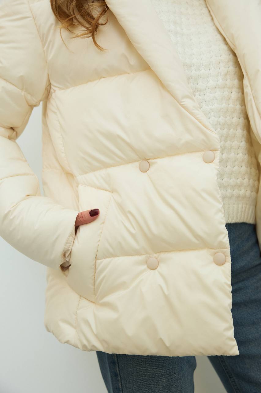 Close-up of a person wearing a cream puffer jacket with a plain background