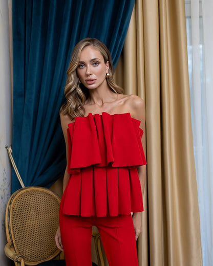 A woman models a bright red off-the-shoulder ruffled top and matching red pants in front of blue and beige curtains.