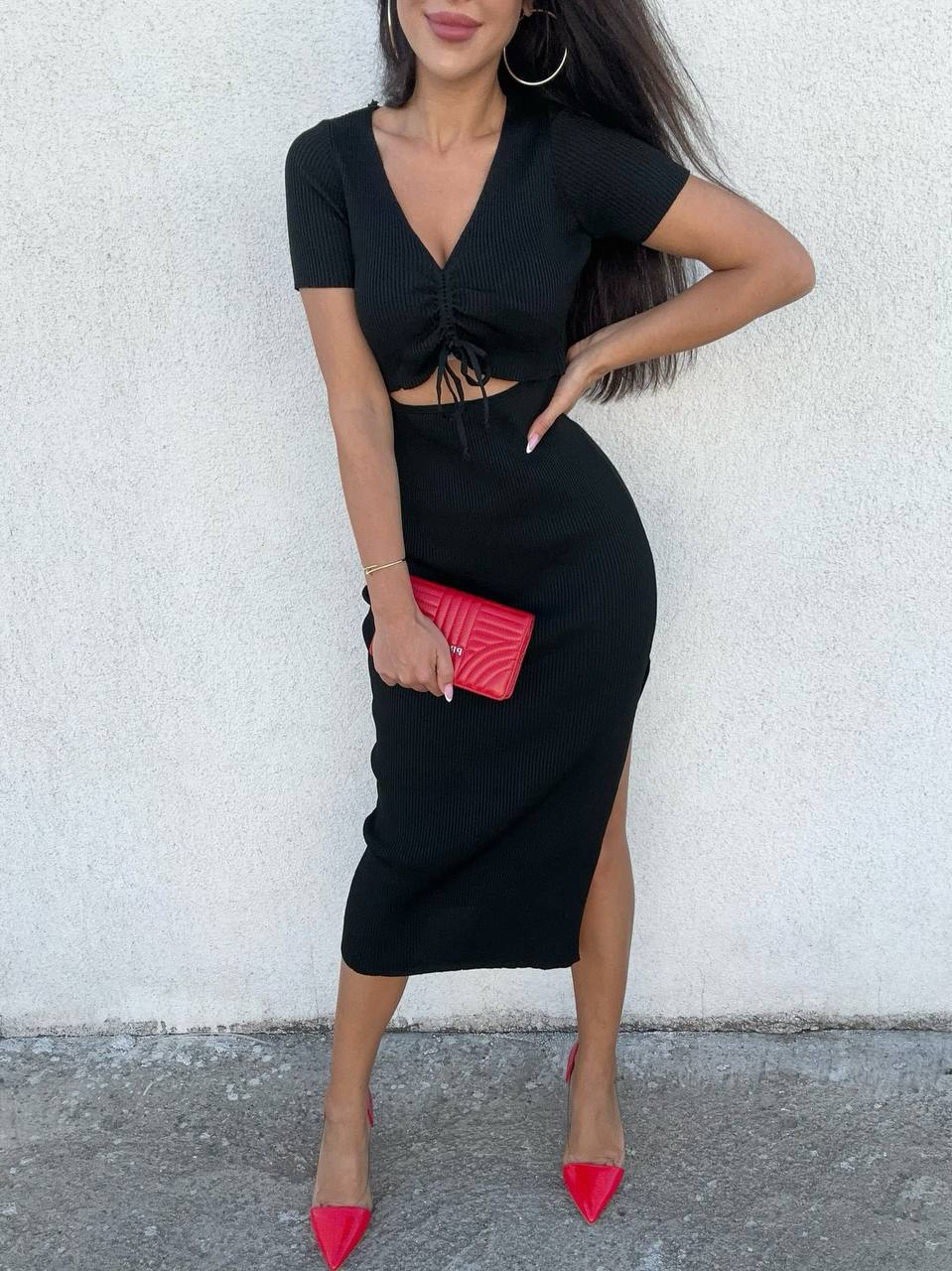 Woman wearing a black dress with a red clutch against a white wall