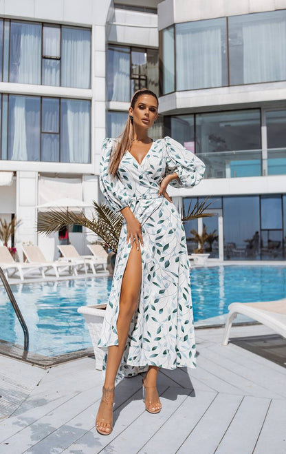 Woman in a white dress with green patterns standing by a poolside.