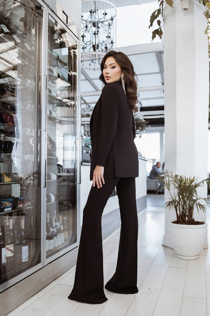 Woman in a black outfit standing in a modern indoor setting with glass walls and plants.