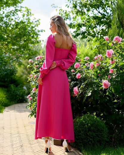 Woman in a pink dress standing in a garden with flowers and greenery.
