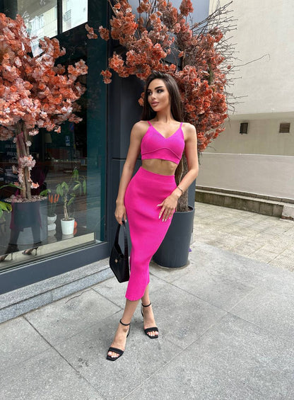 Woman in a bright pink outfit standing on a sidewalk with cherry blossom trees in the background.