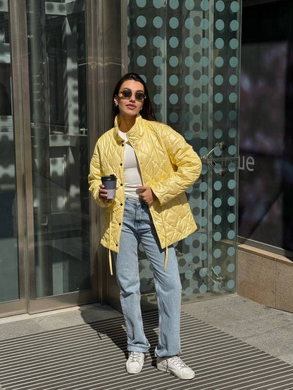 Woman in a yellow jacket and light blue jeans standing in front of a glass door.