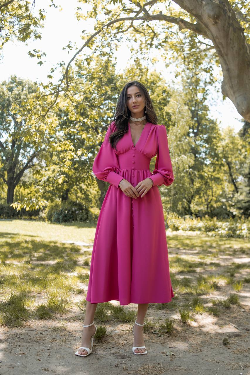 Woman in a pink dress standing in a park with trees and grass in the background