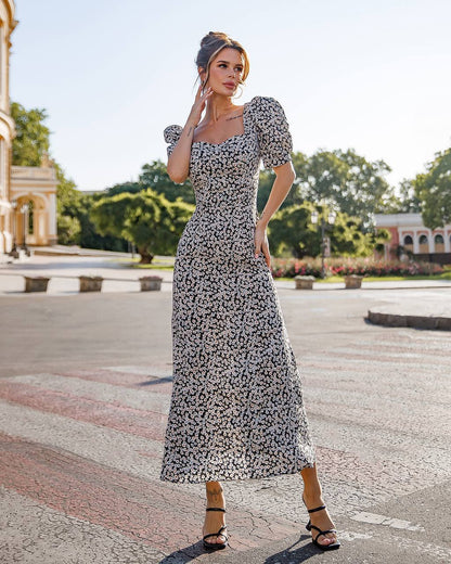 Woman in a floral dress standing outdoors with trees and buildings in the background