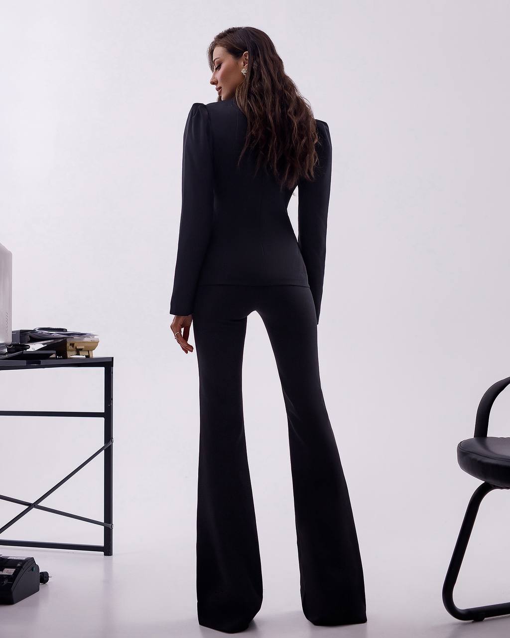 Person wearing a black suit with flared pants in a minimalistic setting