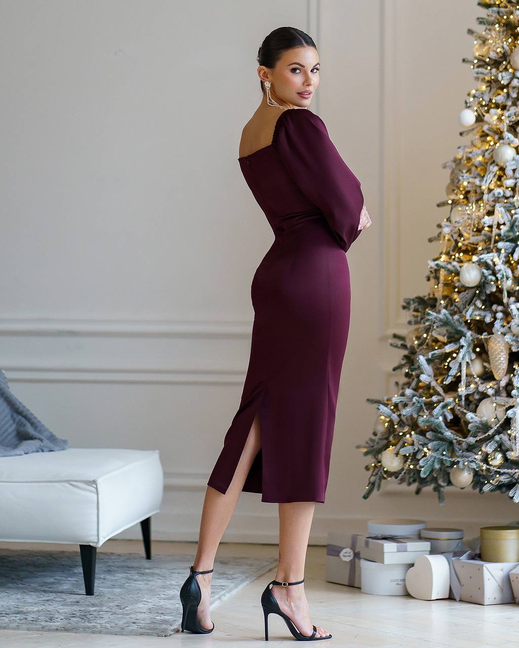 Woman in a burgundy dress standing in a room with a decorated Christmas tree.