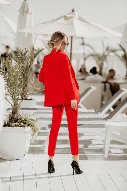 Woman in a red outfit standing on a sunlit deck with plants and people in the background