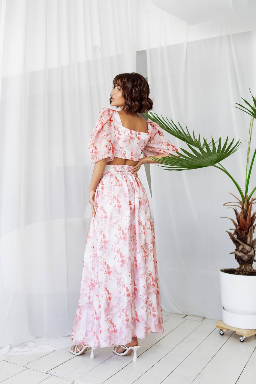 Woman in a floral dress standing in a room with white walls and a plant.