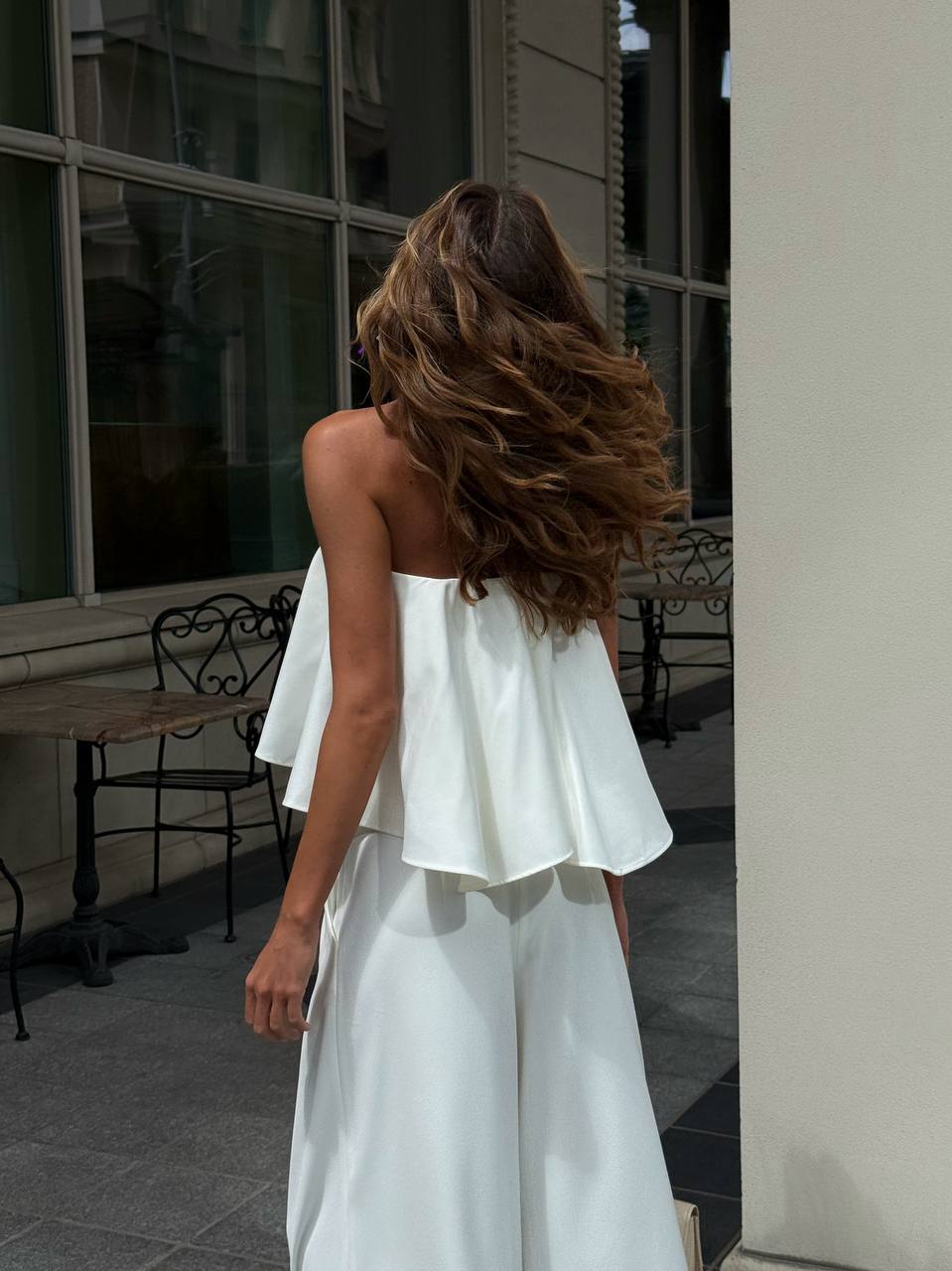 Woman in a white strapless top and skirt standing outdoors.