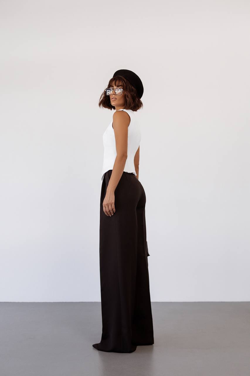 Woman wearing a white sleeveless top and black flowing pants against a white background