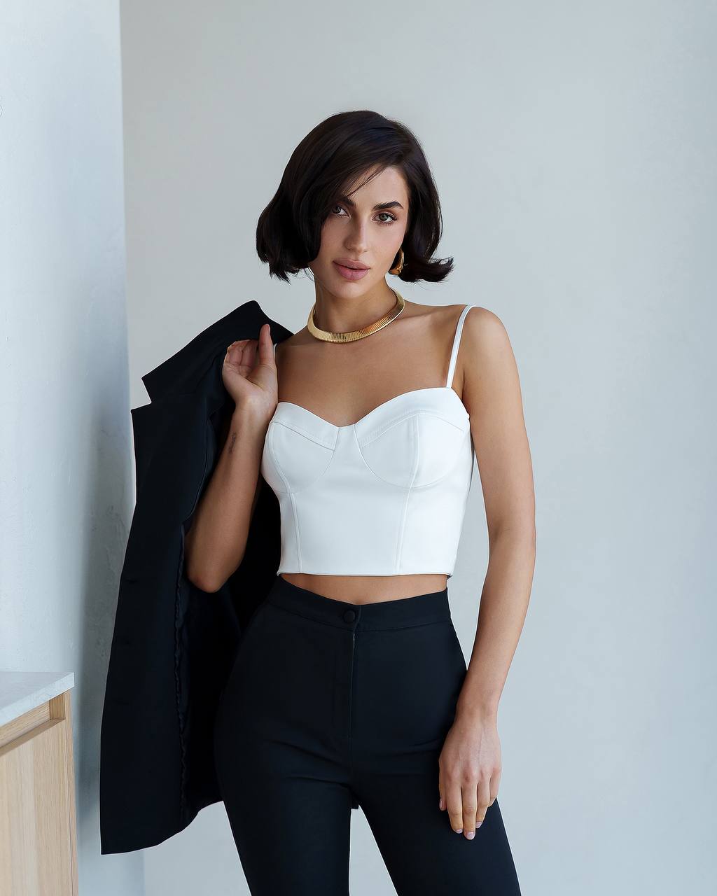 Woman wearing a white top and black pants against a plain background
