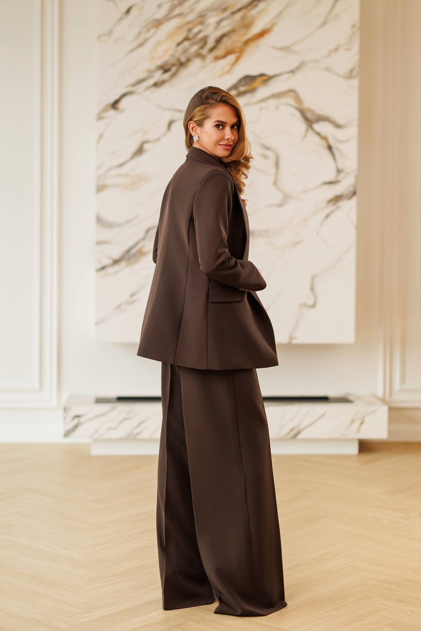 Woman in a brown suit standing in front of a marble wall.