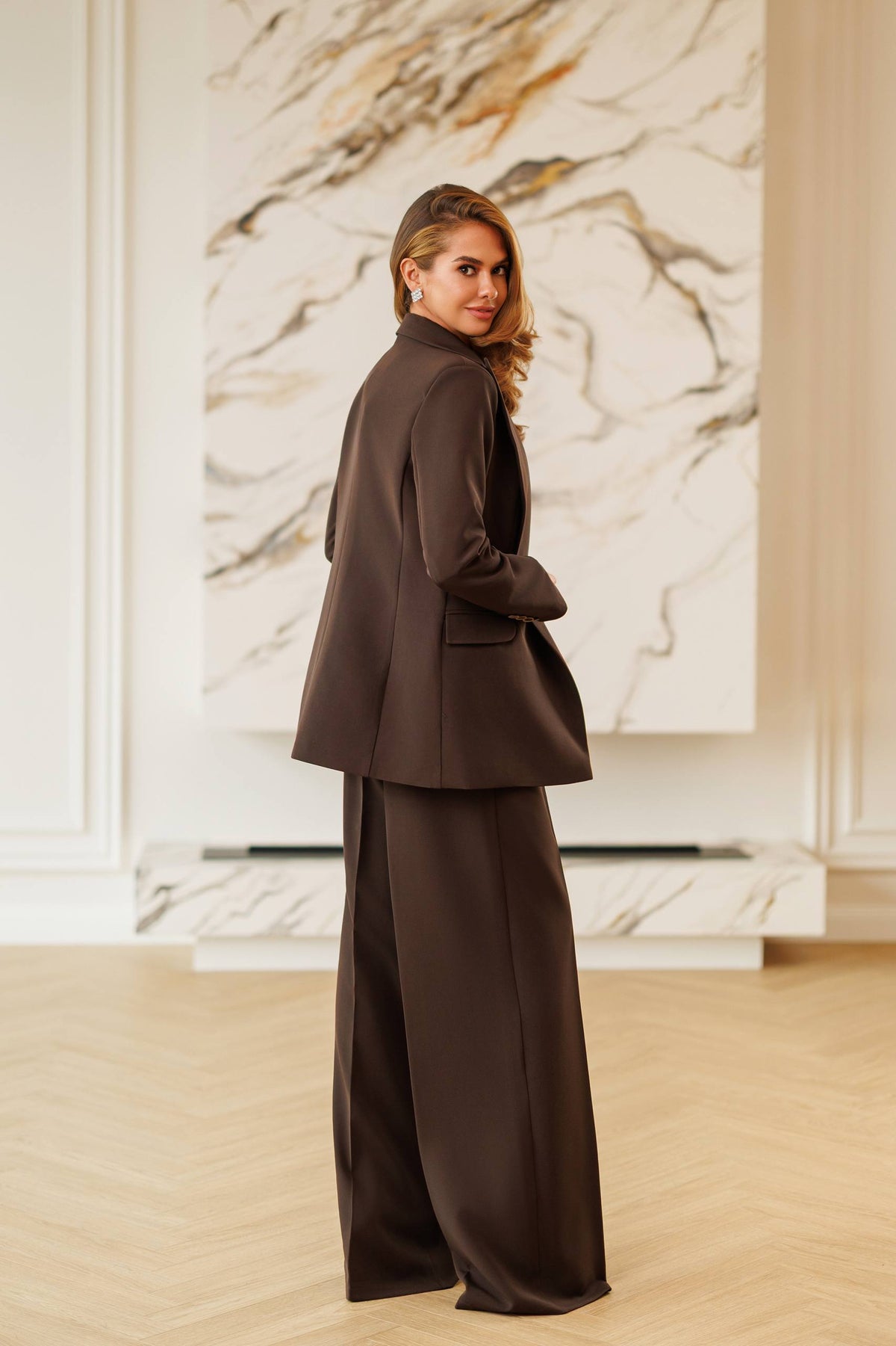 Woman in a brown suit standing in front of a marble wall.