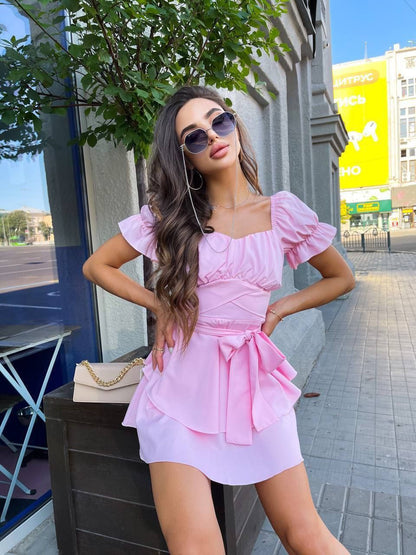 Woman in a pink dress posing outdoors with sunglasses on.