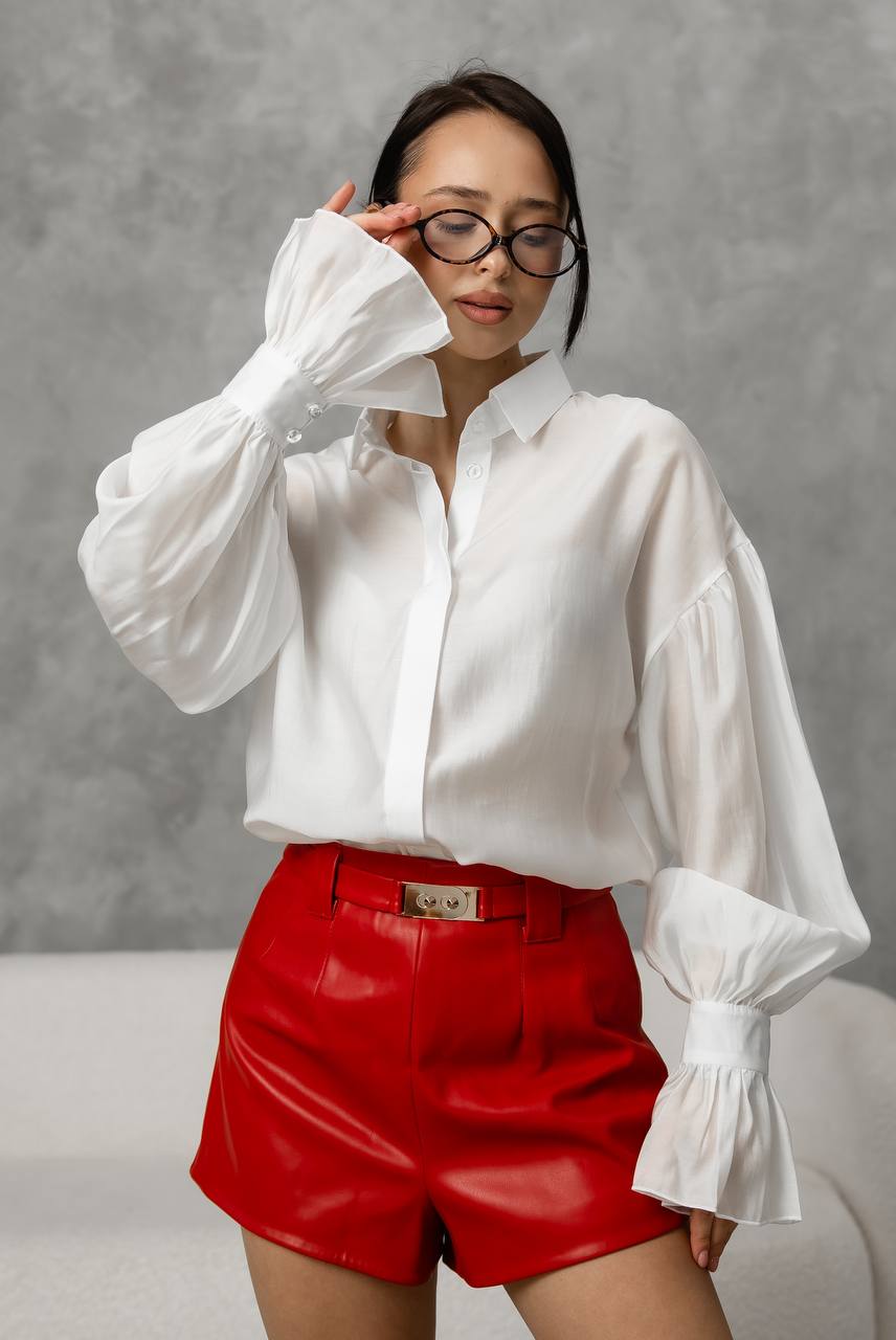 Person wearing a white blouse and red shorts against a gray background