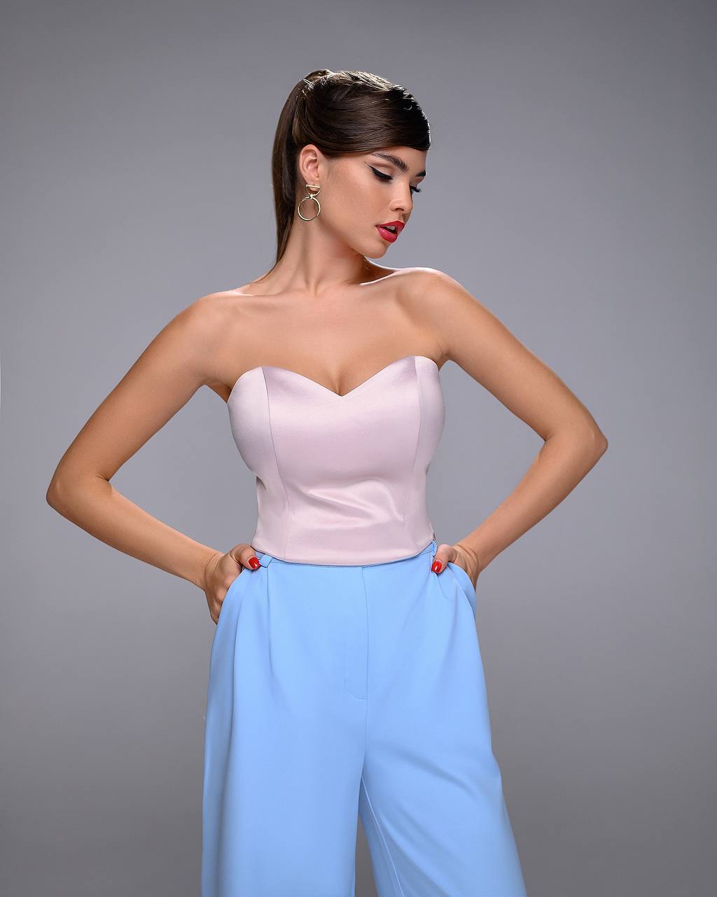 Woman wearing a strapless pink top and light blue pants against a gray background
