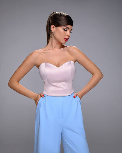 Woman wearing a strapless pink top and light blue pants against a gray background