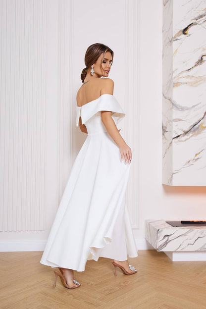 Woman in a white off-shoulder dress standing in a room with marble wall.