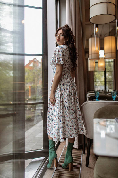 Woman in a floral dress standing by a large window in a modern interior setting.