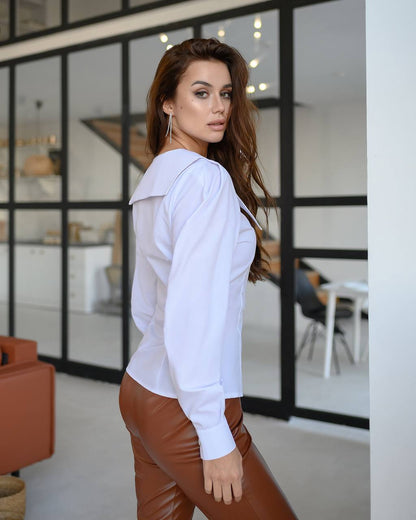 Woman wearing a white blouse and brown pants in an indoor setting