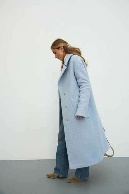 Person wearing a light blue coat with a white interior, standing against a plain background.