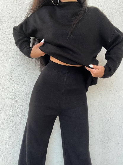 Person wearing a black cropped hoodie and black pants against a light gray background